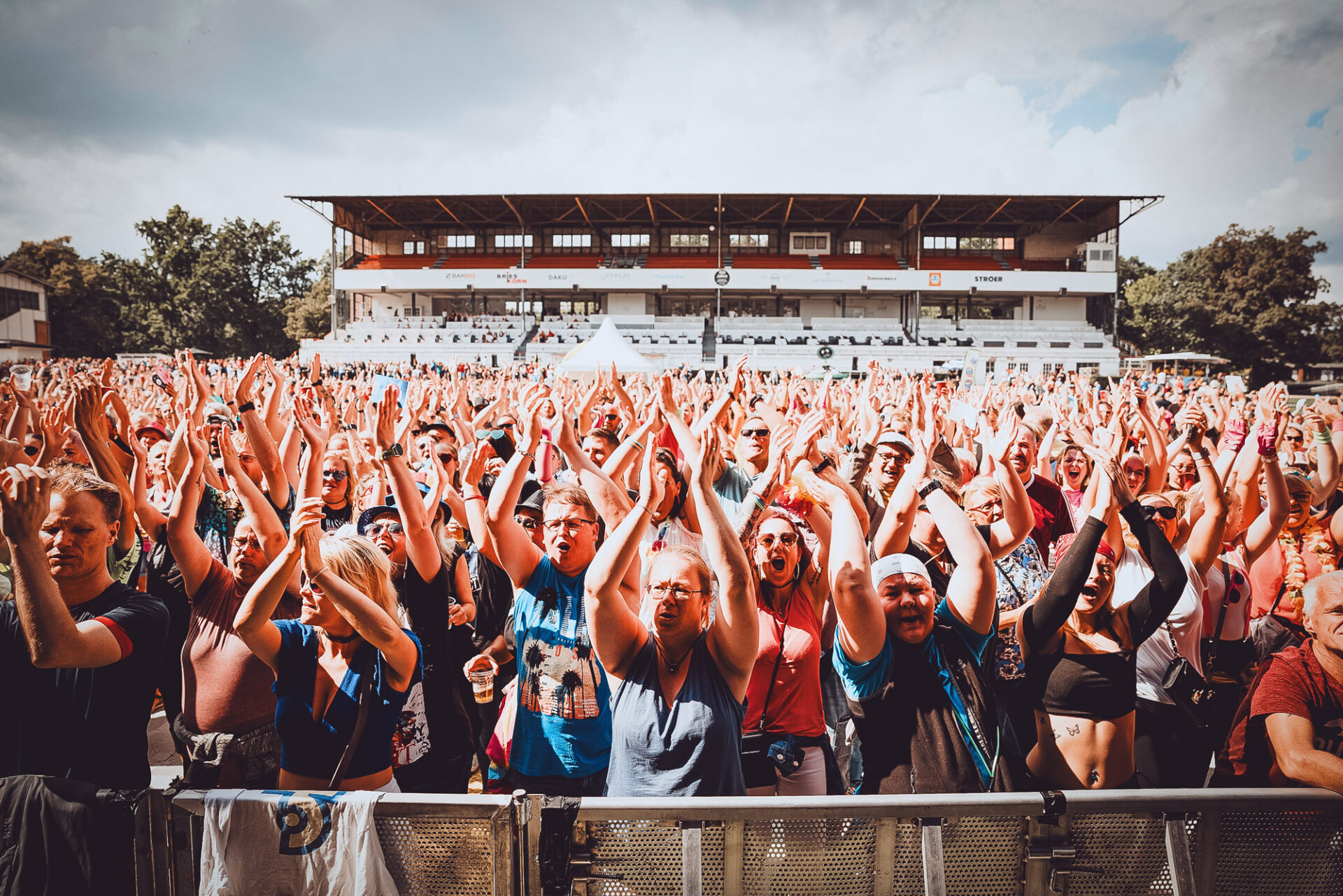 Jubelndes Publikum beim 90er-Festival in Hoppegarten bei Sonnenschein vor der Haupttribüne.