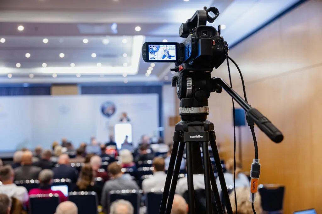 Professional camera on a tripod, ready to record a conference presentation.
