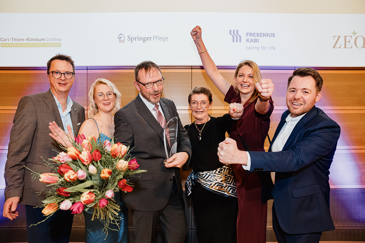 Strahlendes Siegerteam bei einer Gala-Preisverleihung des Pflegeawards, mit Pokal und Blumenstrauß, feiernd vor einer festlichen Kulisse.