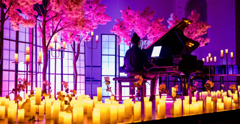 Eventfotografie-Aufnahme eines Konzerts von Dreamlight, bei dem Anime-Musik auf dem Klavier gespielt wird. Der Pianist sitzt vor einem Flügel von Steinway & Sons, während bunte Beleuchtung in Lila und Blau sowie Kerzen im Vordergrund eine stimmungsvolle Atmosphäre schaffen.